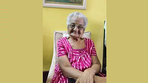Image of Dr. K. Lakshmi Bai wearing a pink dress, sitting and smiling while posing.