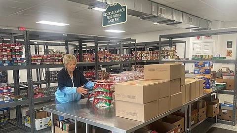 Image of a woman standing in a warehouse surrounded by stacked boxes of food.
