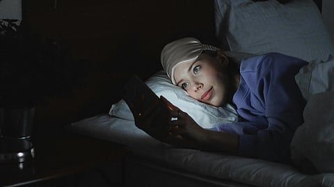 A woman lying in bed and scrolling her phone at night.