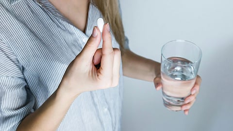 Image of a girl taking a white tablet with a glass of water.