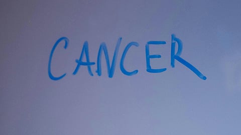 The word "cancer" written in blue marker on a board.