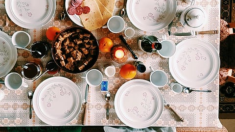 Image of a dining table set with white plates, cutlery, sauces, and bottle of alcohol.