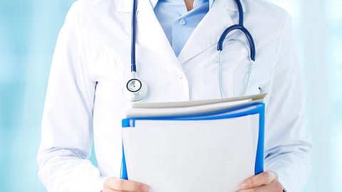 Close-up of a doctor wearing a white coat and stethoscope, holding documents.