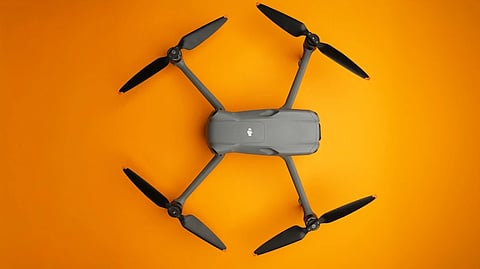 An aerial view of a stationary dark grey drone with four rotors placed on a sunset-yellow backdrop