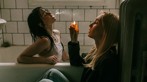 An image of two women sitting in a bathtub, one holding a lighter and other one is smoking.