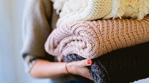 An image of a woman holding a colorful stack of sweaters.