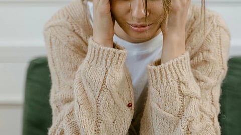 Image of a girl wearing a light brown cardigan and a white t-shirt, appearing very sad.