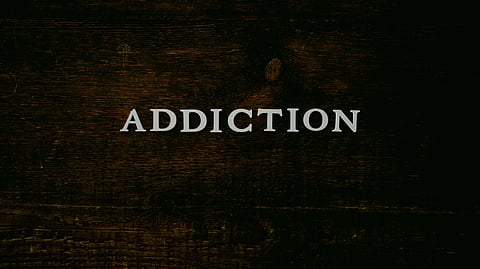 The word "addiction" is prominently displayed on a textured wooden background.