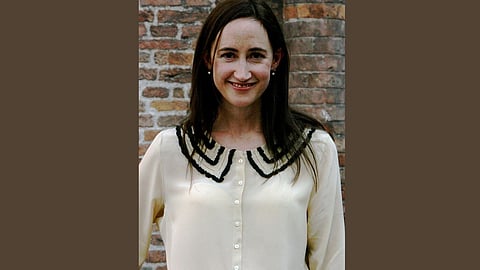 Image of Sophie Kinsella wearing a white sweater, smiling while standing in front of a wall.
