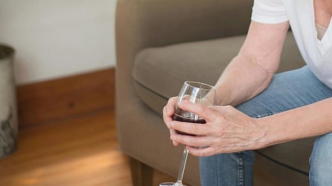 Image of a person wearing blue jeans and a white T-shirt, holding a glass of wine while sitting on a sofa.