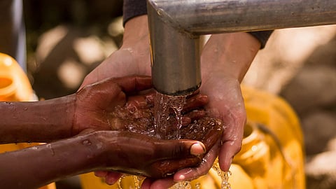 Hands of two people, gather water from a metal spout.