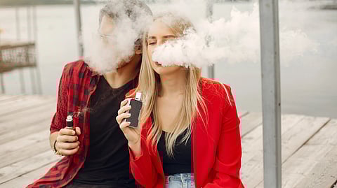 An image of a man and woman siting on a dock, sharing a moment while using an electronic cigarette together.