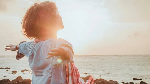 Image showing a woman standing by the sea with open arms embracing the warmth of the sun and feeling freedom from her disease, trigeminal neuralgia.