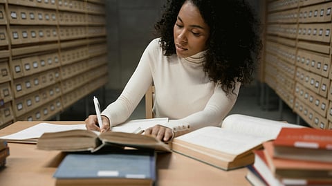 Image of a woman wearing a white top and writing her very first research paper.