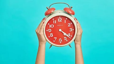 An image of a person holds an alarm clock against a blue background.