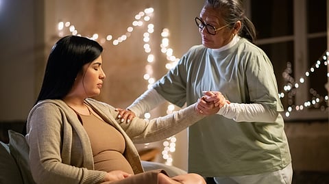 An image of a woman gently holds the hand of pregnant woman.