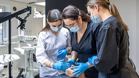 Three-women students learning and observing a clinical case on a patient on a dental chair. 