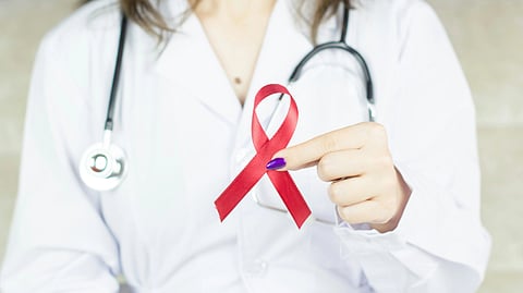 A doctor in a white coat holds a red awareness ribbon, symbolizing support for HIV/AIDS causes.
