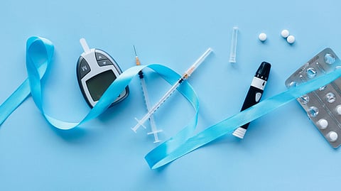 An image of diabetes-related items, glucometer, insulin syringes, lancet, pills, blister pack, and a blue ribbon.