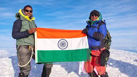 An image showing the doctor couple holding the tricolor Indian flag on snow at a mountain peak.