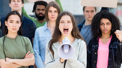 An image of diverse group of young people protesting, woman in a center shouts into a megaphone.