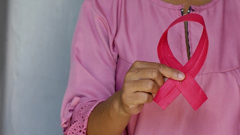 An image of woman in a pink shirt holds a pink breast cancer awareness ribbon.