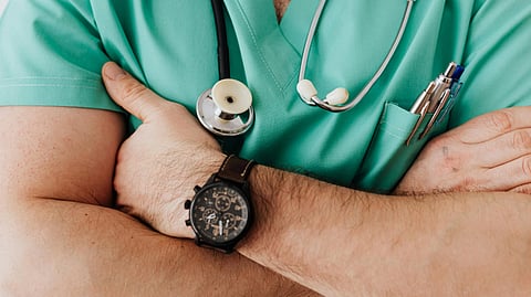 Image of a doctor wearing green scrubs, with a stethoscope and a wristwatch.