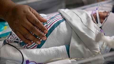 An image of a gentle hand rests on a swaddled baby in a hospital crib.