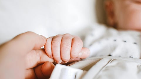 An image of a baby holding a woman's hand.