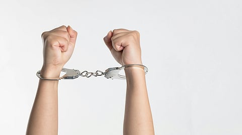 Image showing two hands in metal handcuffs are raised against a white background.