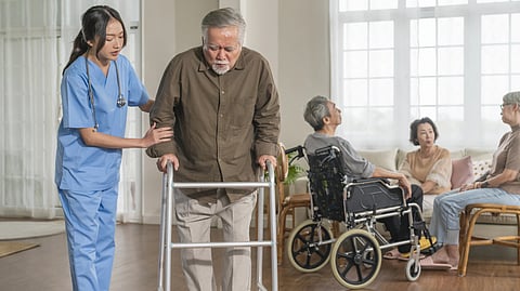 A nurse helping a man walk using a walker.