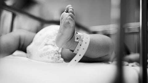 A black and white image of an infant with a hospital tag on leg in focus. 