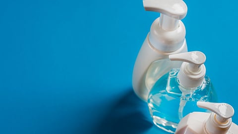 An image of three soap dispensers with white pumps are arranged on a blue background.