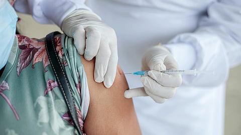An image of healthcare worker in white gloves administers a vaccine to a person in a floral shirt.