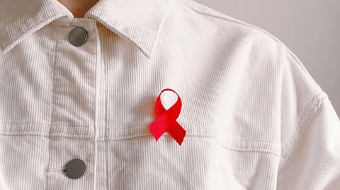 An image of close-up of a person wearing a white button-up shirt adorned with a red awareness ribbon.