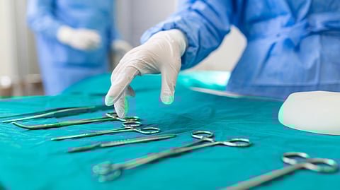 An image of healthcare professional in blue scrubs and gloves selects a surgical tool from a table.