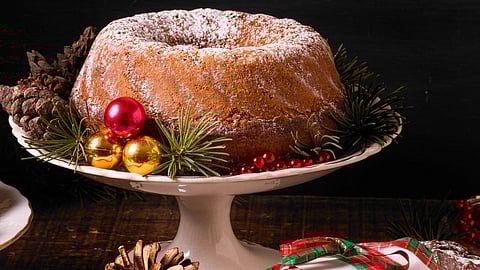 An image of festive cake dusted with powdered sugar sits on a white stand, surrounded by red and gold ornaments.