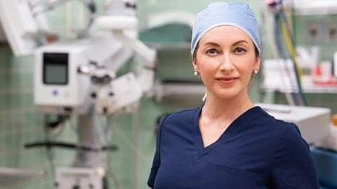 An image of confident female medical professional in scrubs and a surgical cap stands in an operating room.