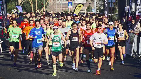 An image of large group of runners at the start of a road race, wearing colorful athletic gear and bib numbers.