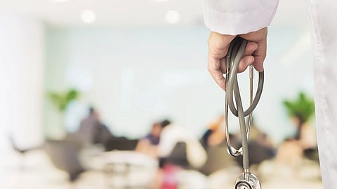 A person wearing a white apron holding a stethoscope in focus.