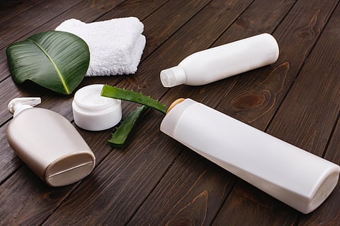 White towel, bottles of shampoo and conditioner lie on a table with green leaf and aloe