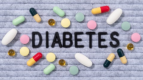 An image of text "DIABETES" surrounded by assorted pills and capsules on a textured gray background.