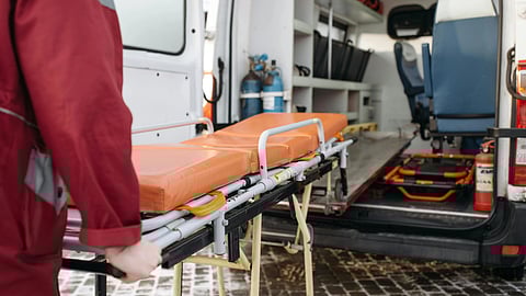 An image of a person in a red uniform pushes an orange stretcher towards an open ambulance.
