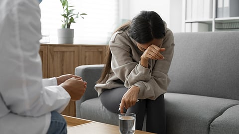 An image of a woman in distress sits on a gray sofa, wiping tears.