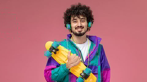 A young man wearing a very colorful jacket with a skateboard in his hand.