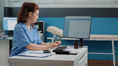 A lady doctor entering some data into a PC at a hospital. 
