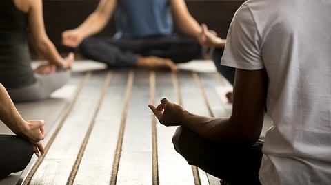 An image of people sitting cross-legged on yoga mats in a calm, indoor setting, with hands on knees in a meditation pose.
