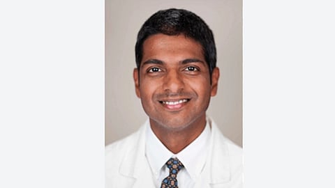 An image of a smiling man in a white coat and patterned tie.