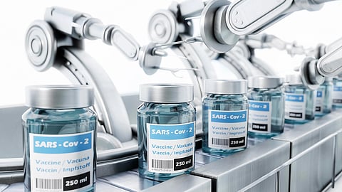 An image of robotic arms handle vials labeled "SARS-Cov-2 Vaccine" on an assembly line.