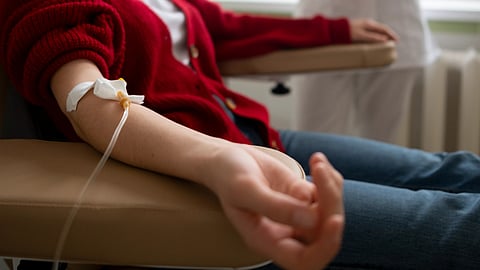 An image of a patient in a red sweater, receives an IV treatment.